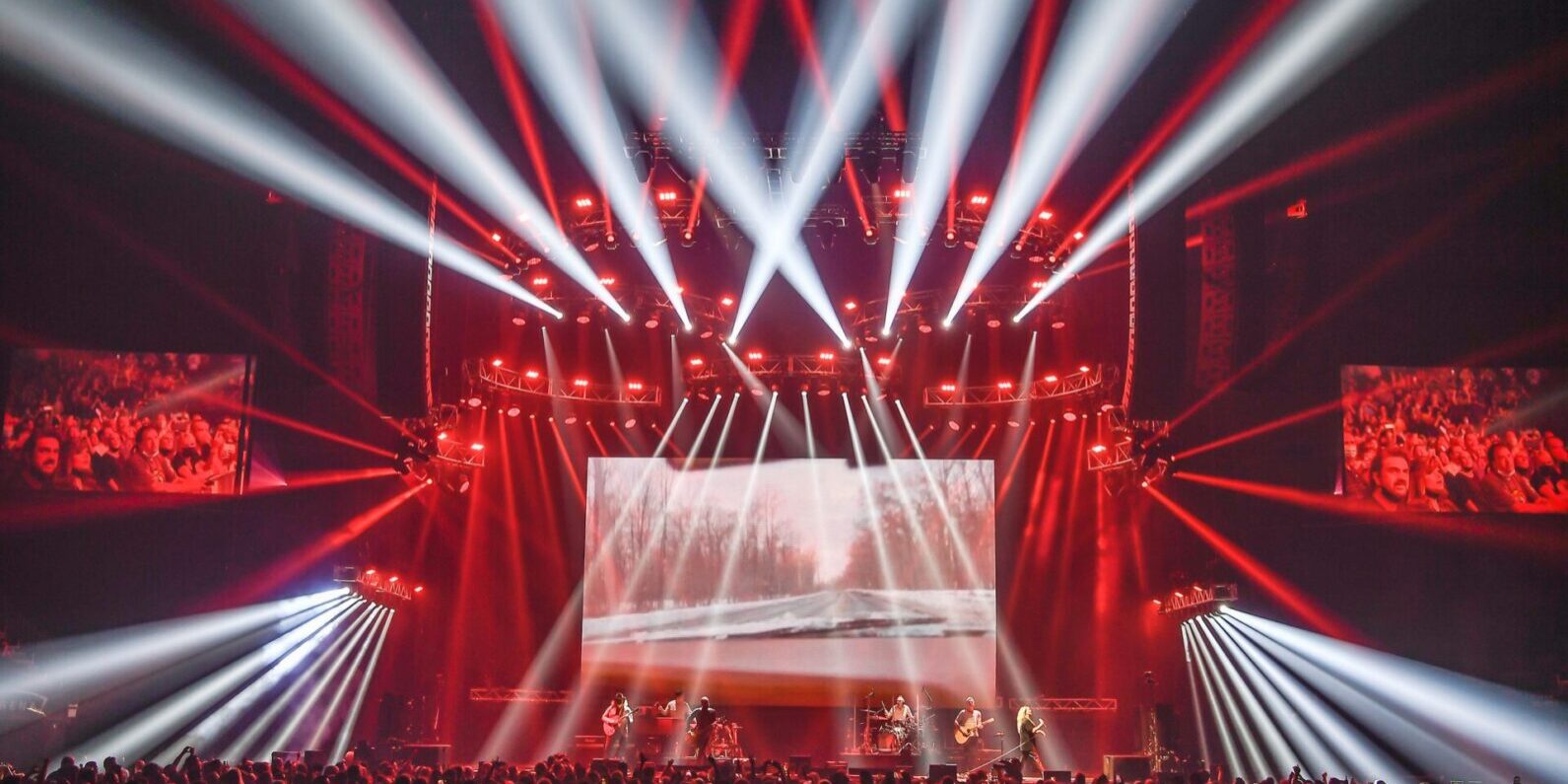 A vibrant concert stage with red and white lights illuminating a large crowd.