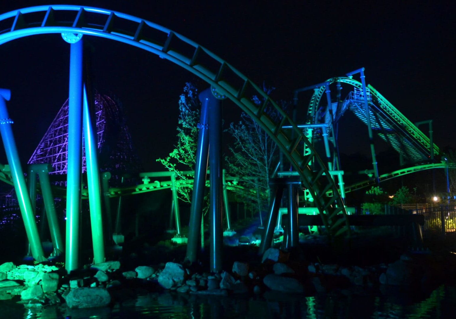 Roller coaster illuminated with green and blue lights at night.