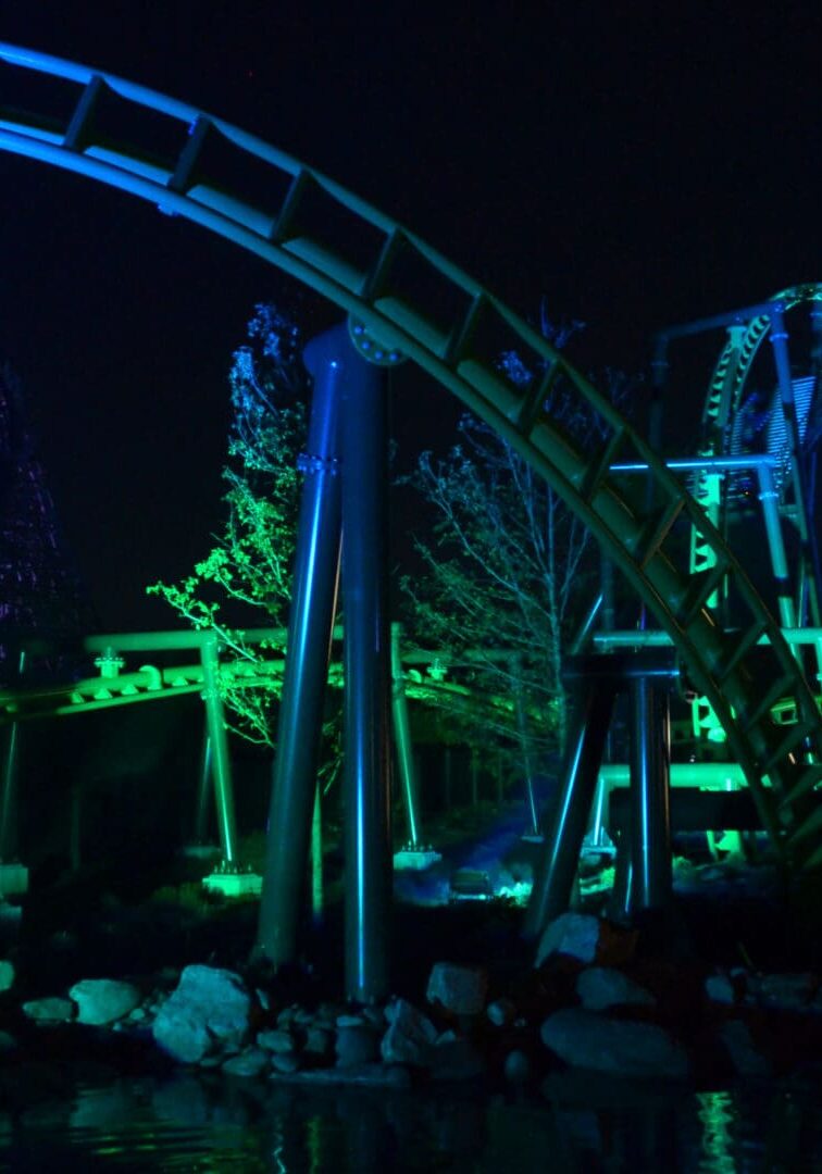 Roller coaster illuminated with green and blue lights at night.