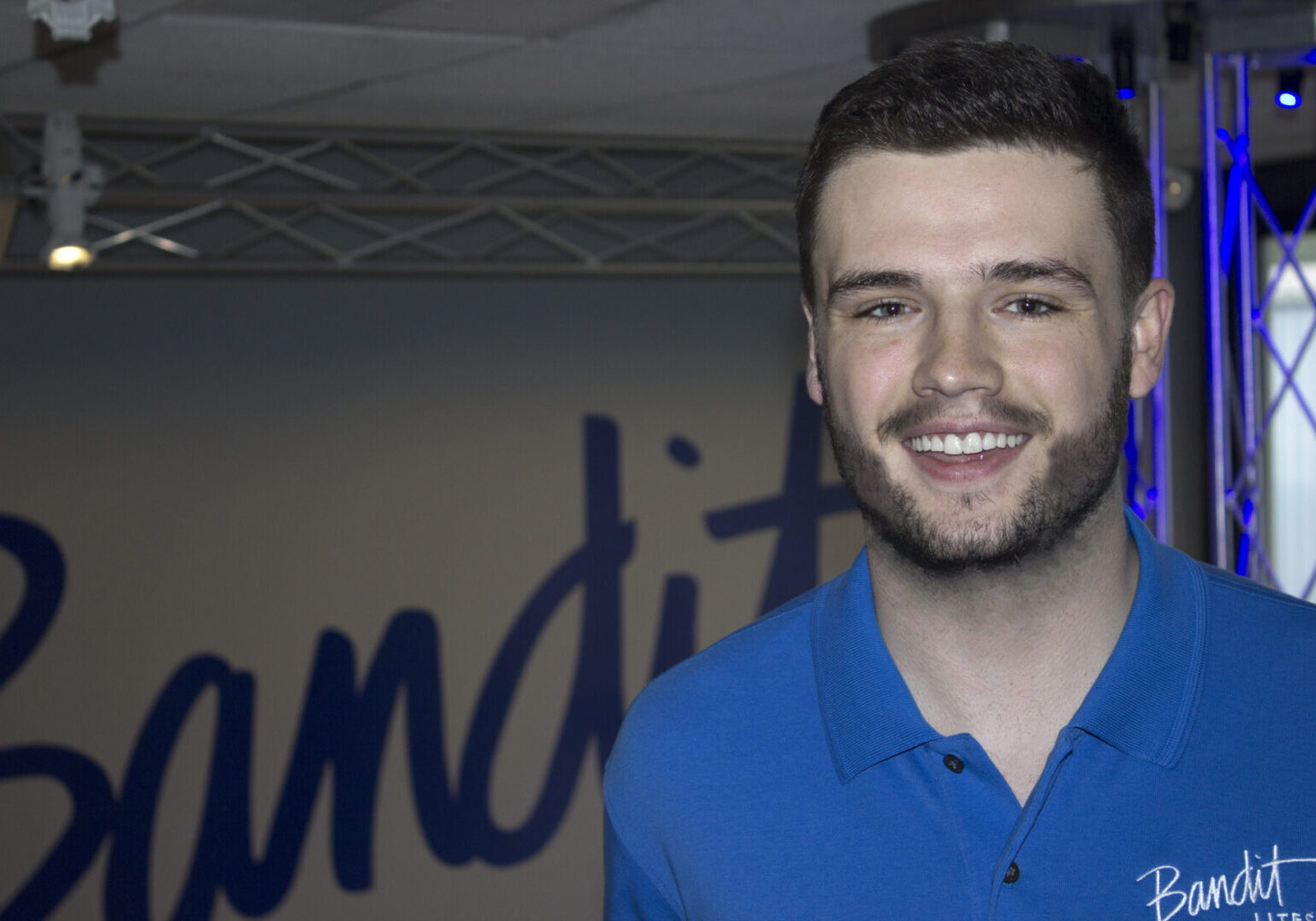 Smiling young man in a blue polo shirt posing indoors.