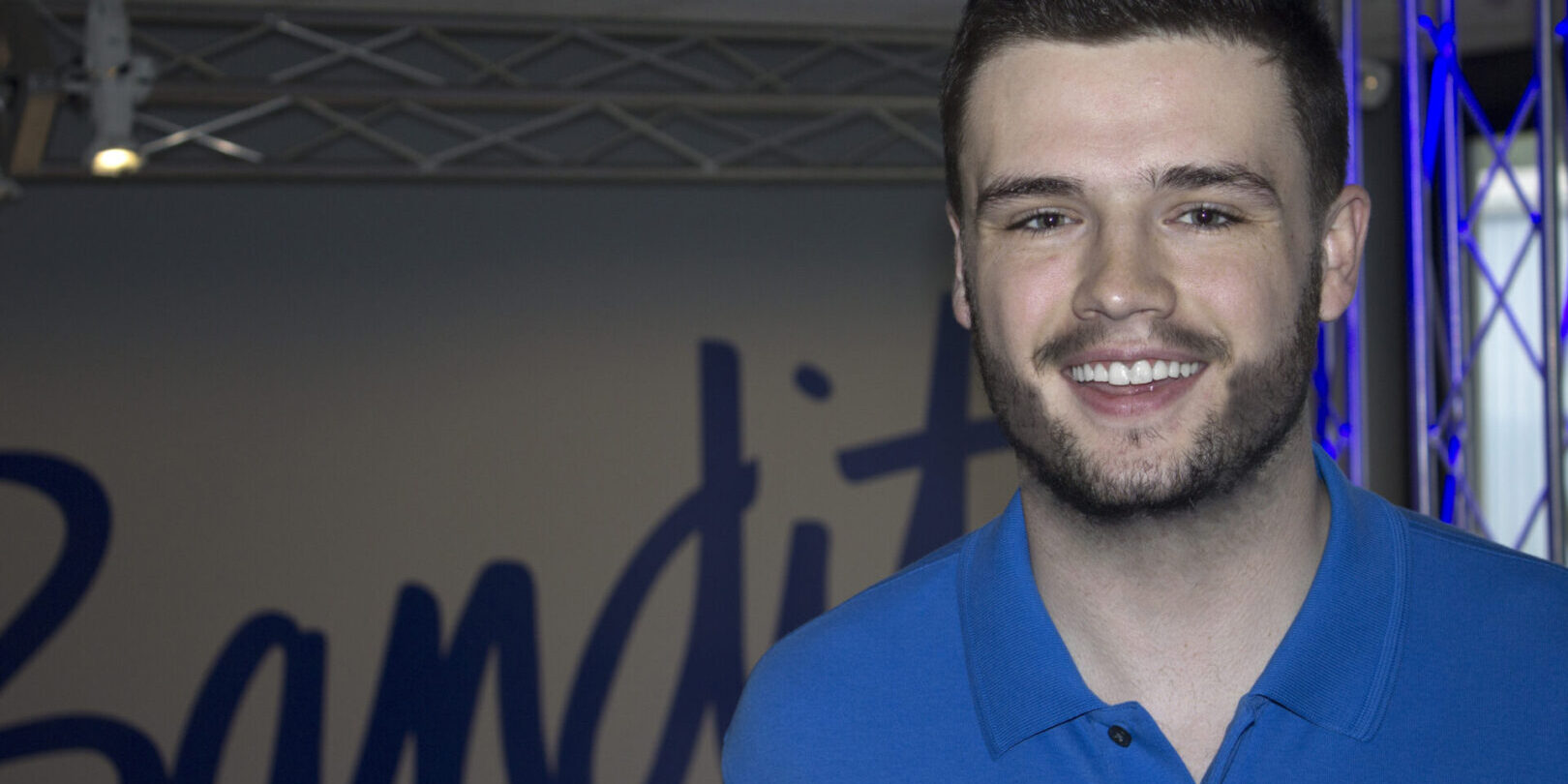 Smiling young man in a blue polo shirt posing indoors.