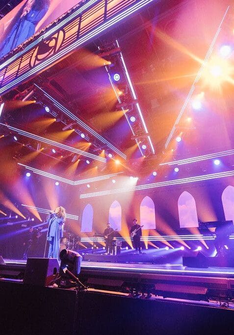 Vibrant stage lighting illuminates a large, modern concert venue.