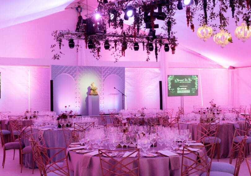 Elegant wedding reception setup with pink lighting and floral chandeliers.