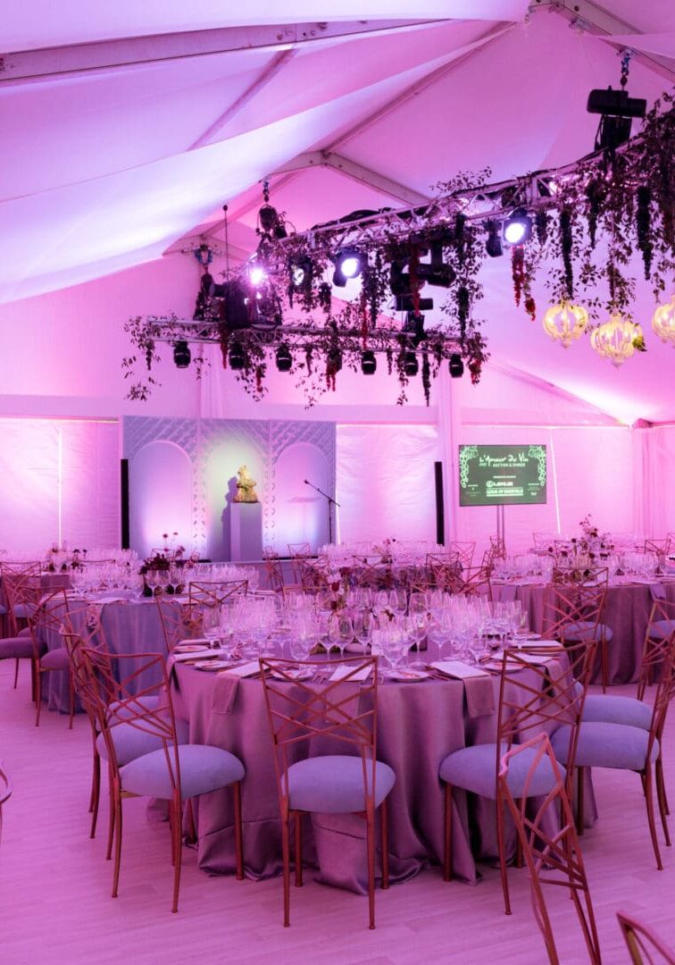 Elegant wedding reception setup with pink lighting and floral chandeliers.