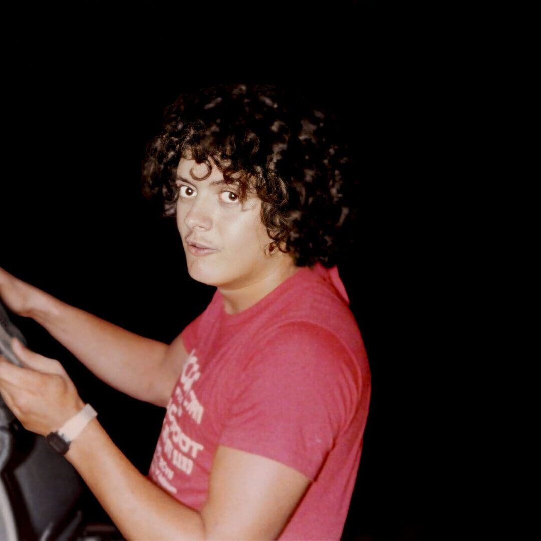 Young person with curly hair wearing a red shirt, holding an object.