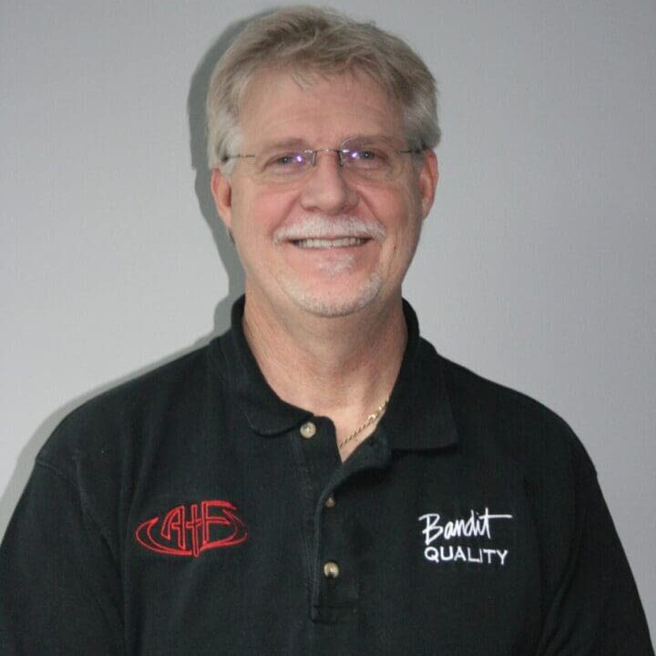Smiling elderly man wearing glasses and a black polo shirt with logos.