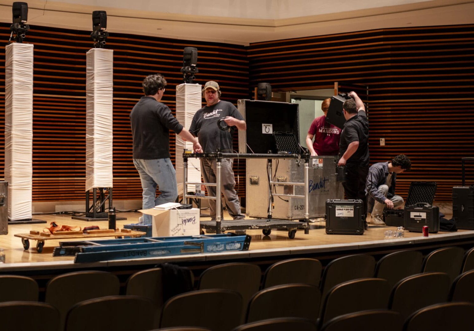 Three men setting up audio equipment in an auditorium.