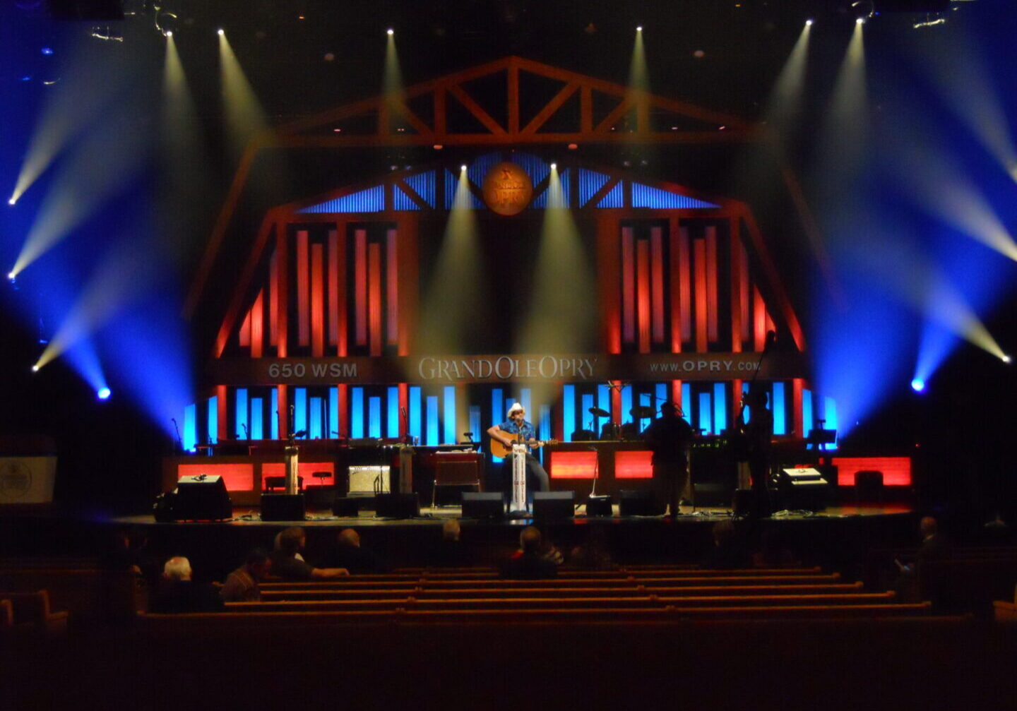 A large stage setup with vibrant blue and red lighting and multiple screens.