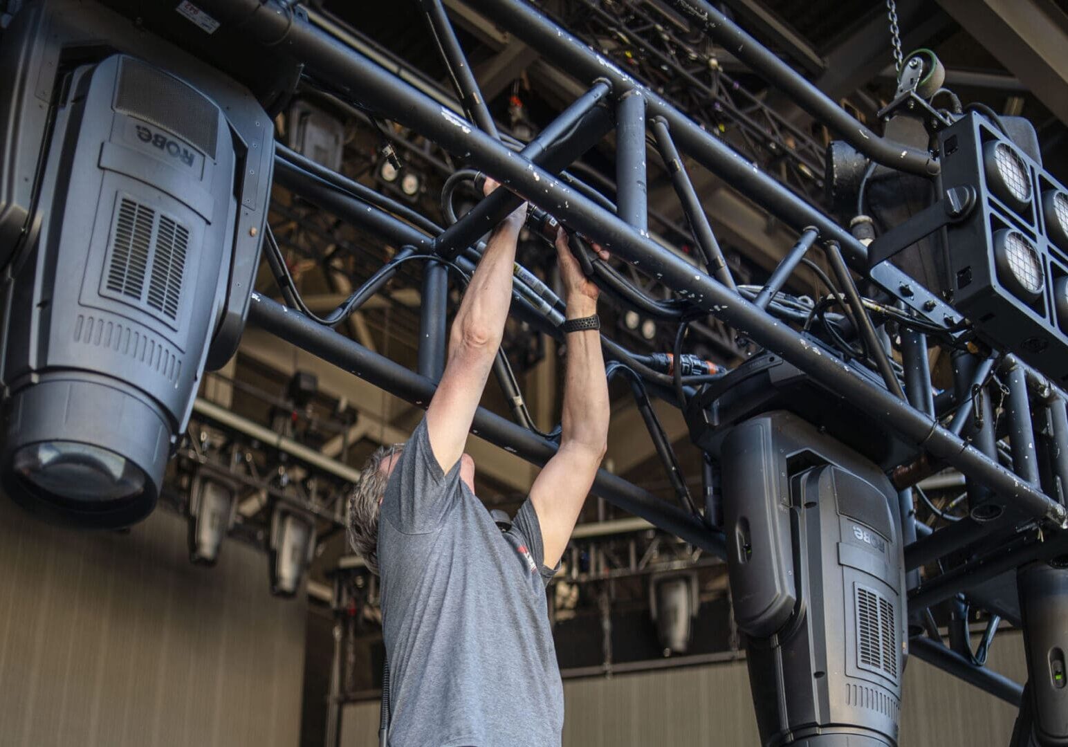 Person adjusting stage lighting on rigging overhead.