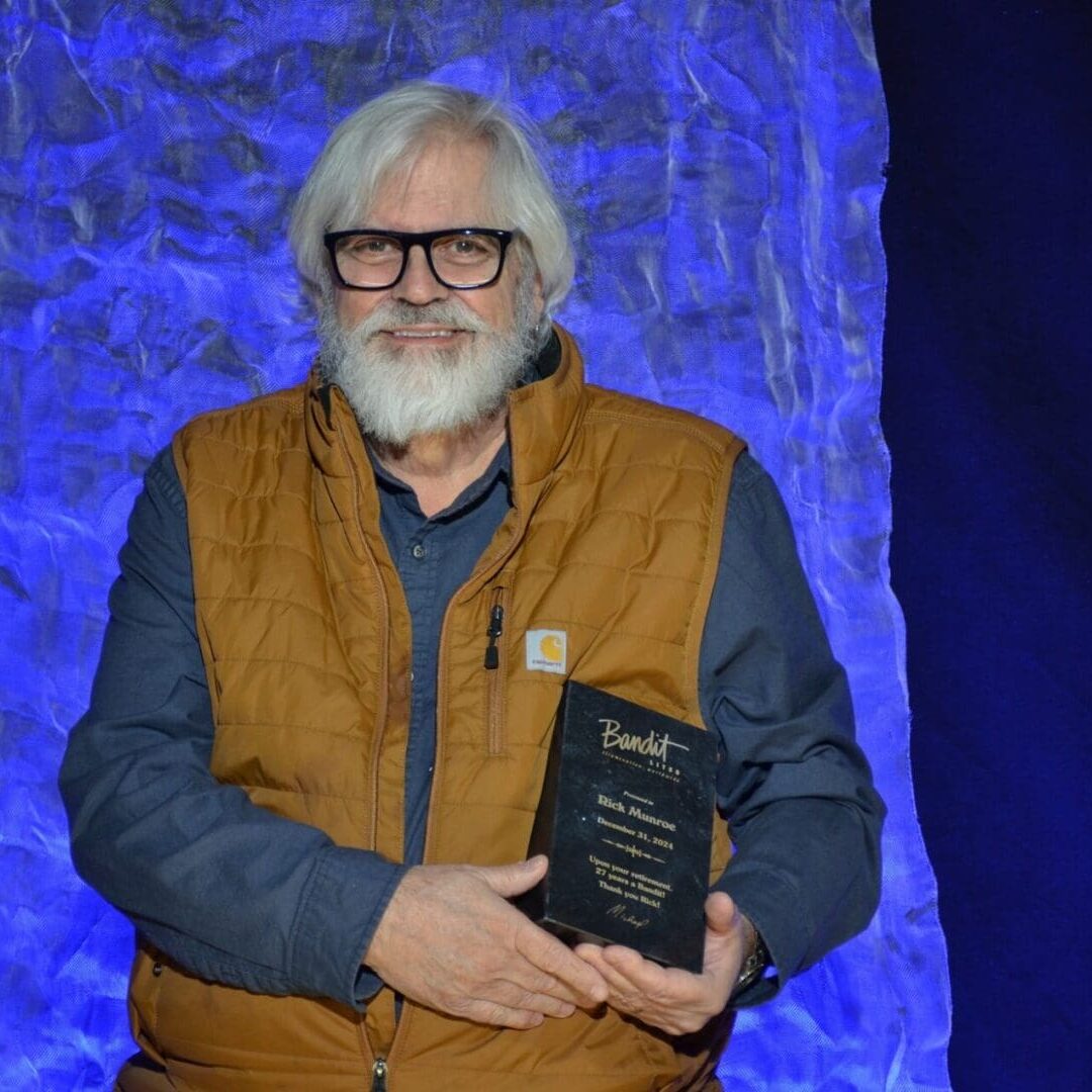 A man with glasses and a beard holding an award plaque, standing against a blue-lit stone wall.