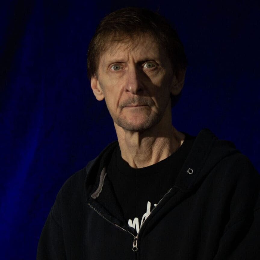 Portrait of a man with a serious expression against a dark blue background.