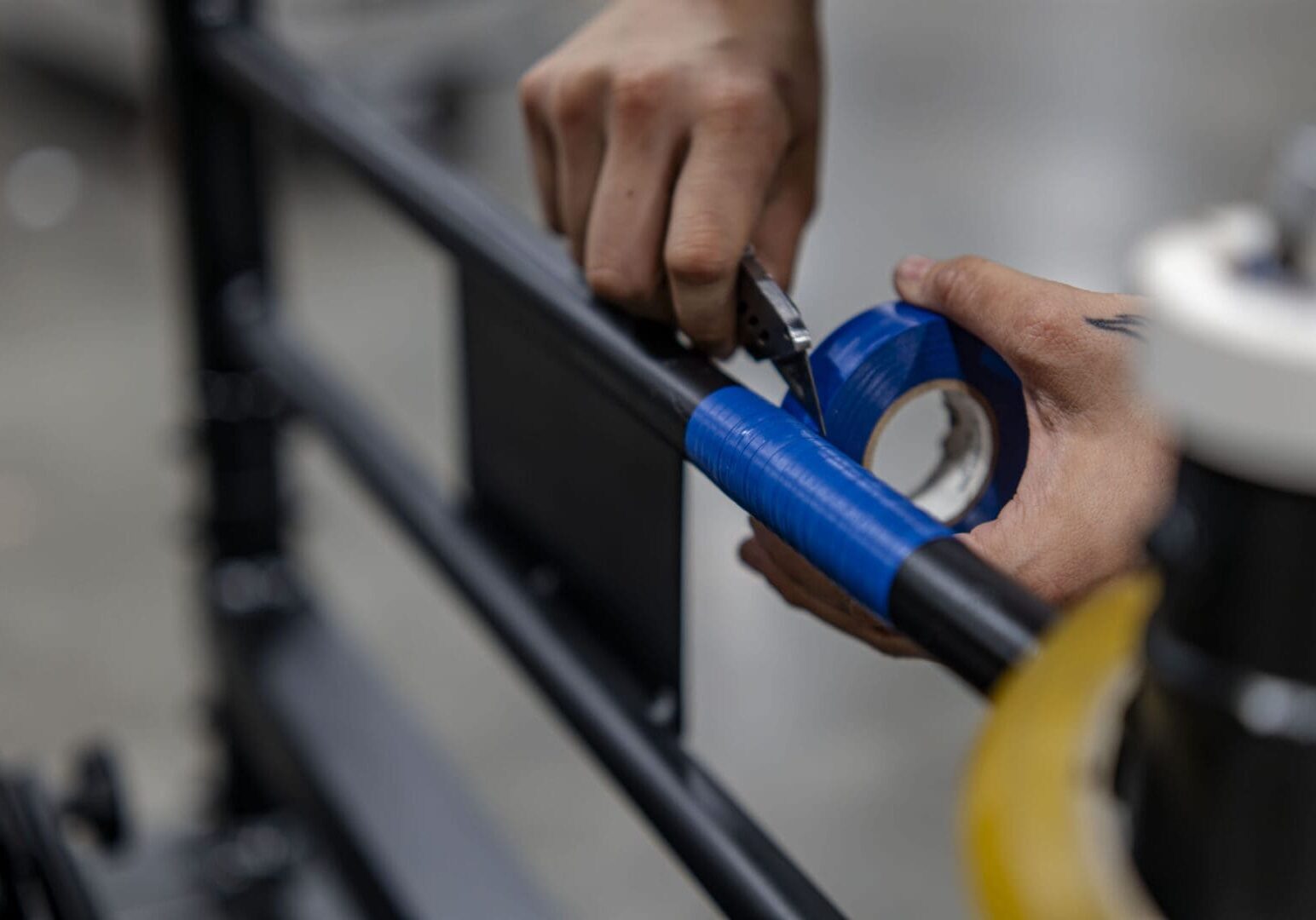 Person wrapping blue tape around a metal railing outdoors.