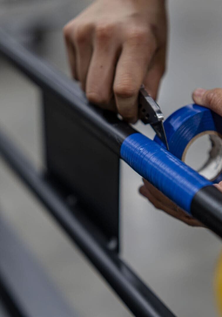 Person wrapping blue tape around a metal railing outdoors.
