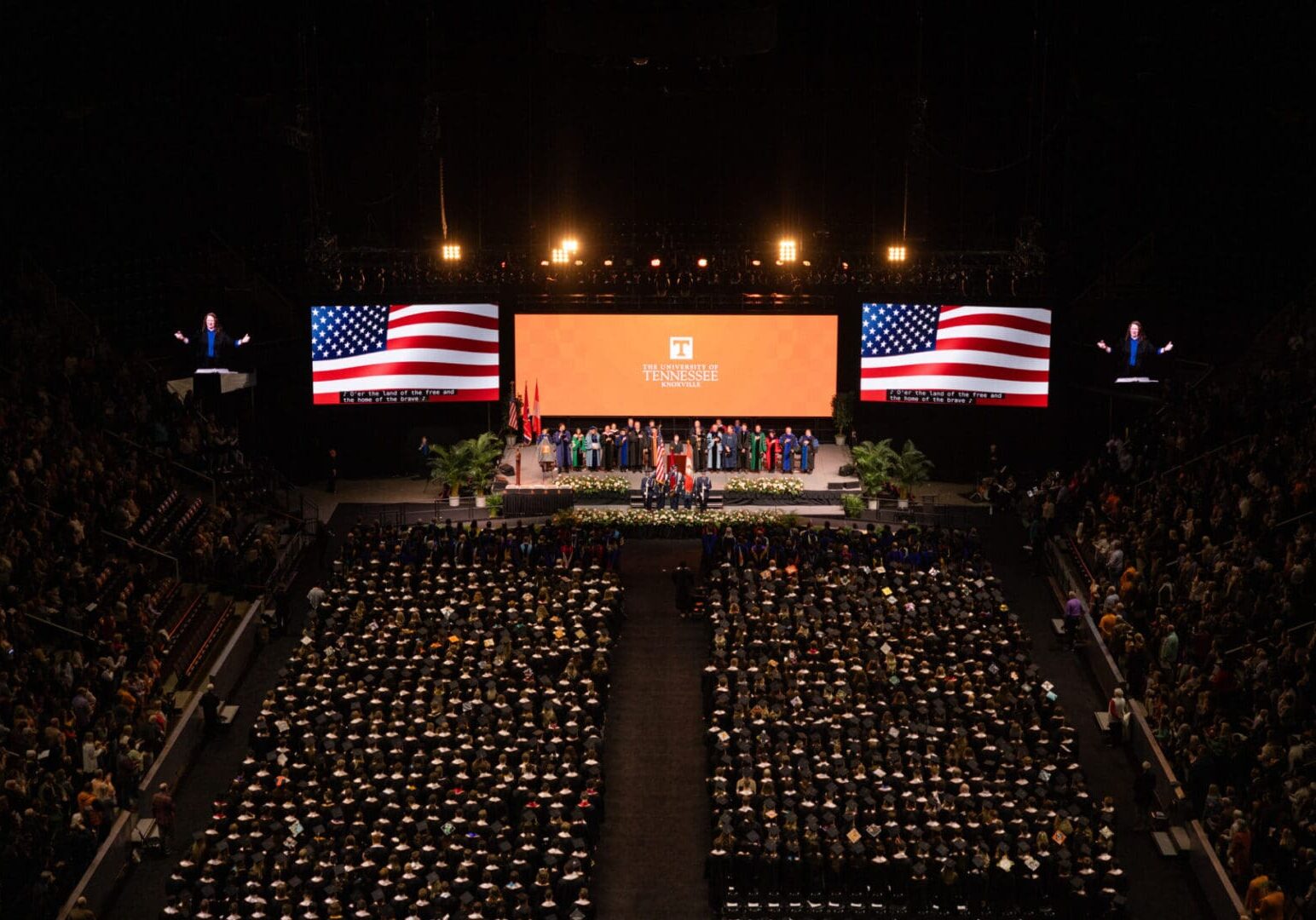 Graduation ceremony with American flags and a large crowd of graduates.