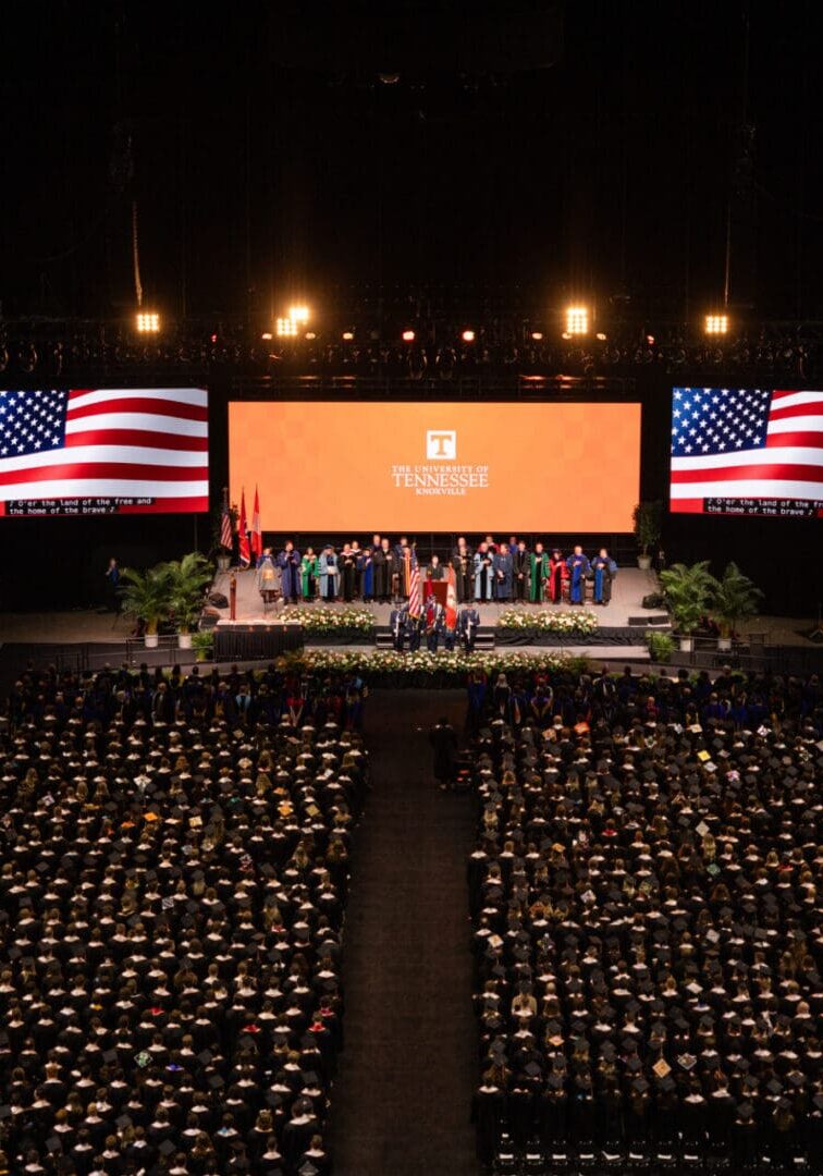 Graduation ceremony with American flags and a large crowd of graduates.