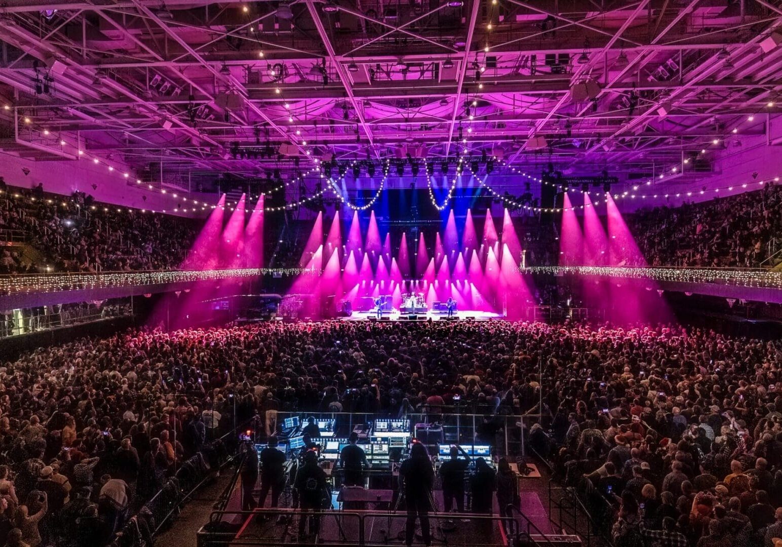 A vibrant concert with bright pink and purple stage lights and a large audience.