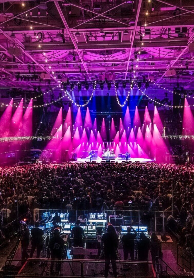 A vibrant concert with bright pink and purple stage lights and a large audience.