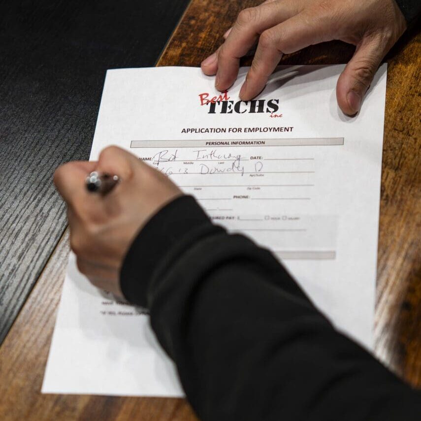 Person signing a printed contract on a wooden table.