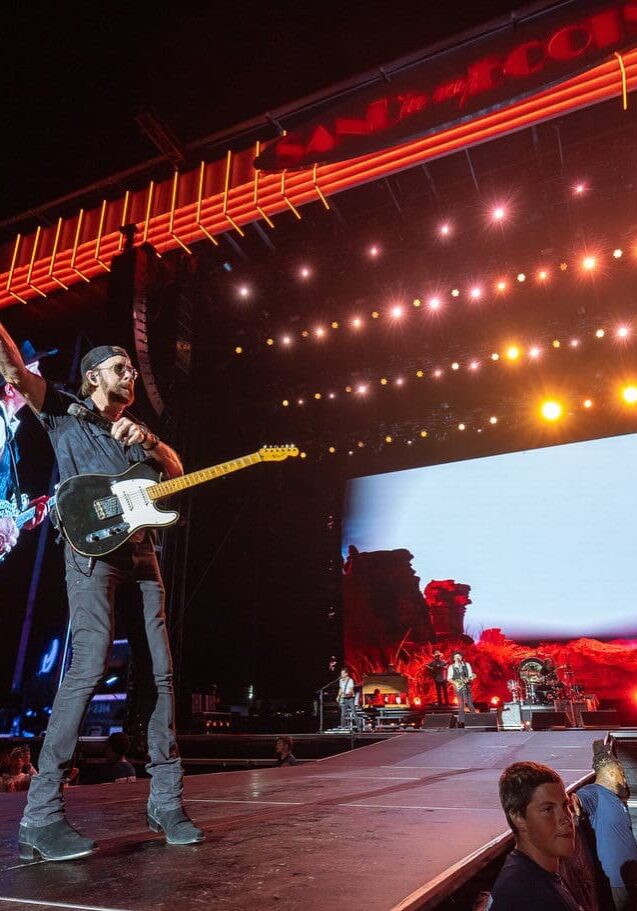 Electric guitarist performing on stage under bright lights.