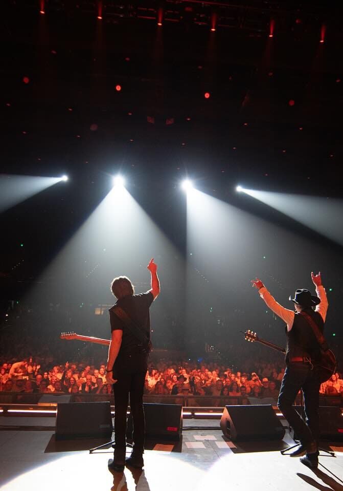 Performers on stage illuminated by spotlights with audience in the background.