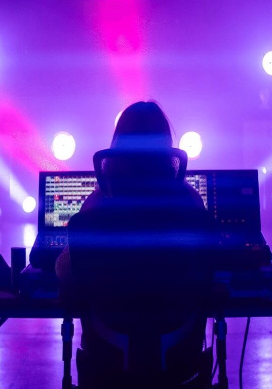 DJ performing live with vibrant purple and blue stage lighting.
