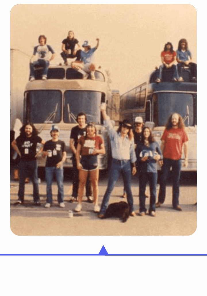 A group of people posing in front of two buses, some wearing matching shirts.