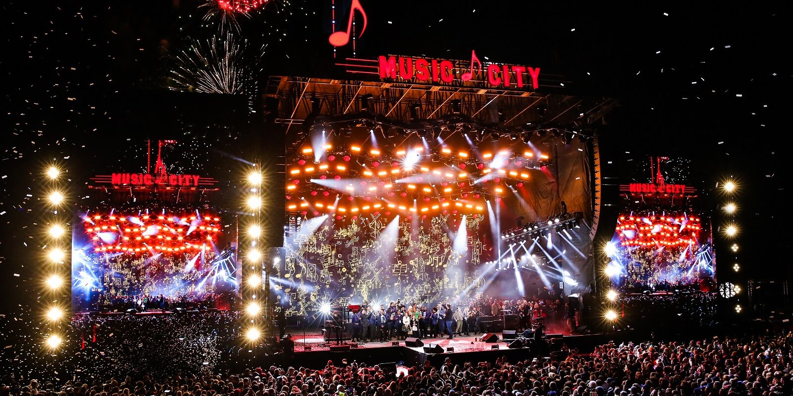 Massive crowd enjoying a vibrant concert with fireworks and bright stage lights.