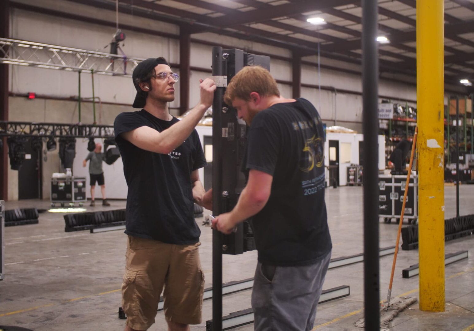 Two men setting up audio equipment in an industrial space.